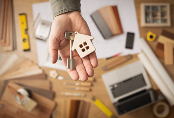 Extended over tools for real estate agents, a hand holds out a key to a new house