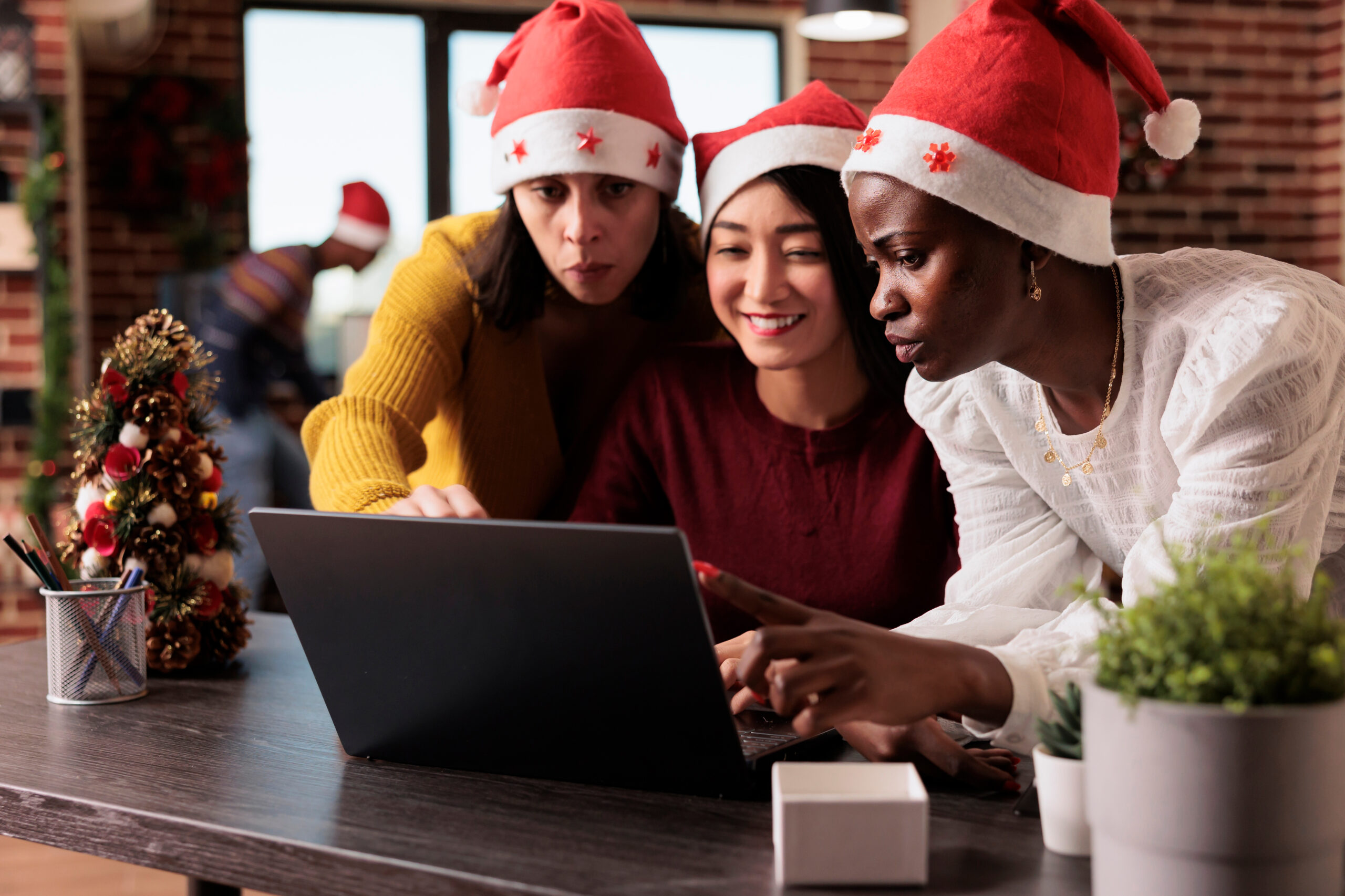 Three co-workers in Santa hats looking at an article about stocking stuffer gifts for work