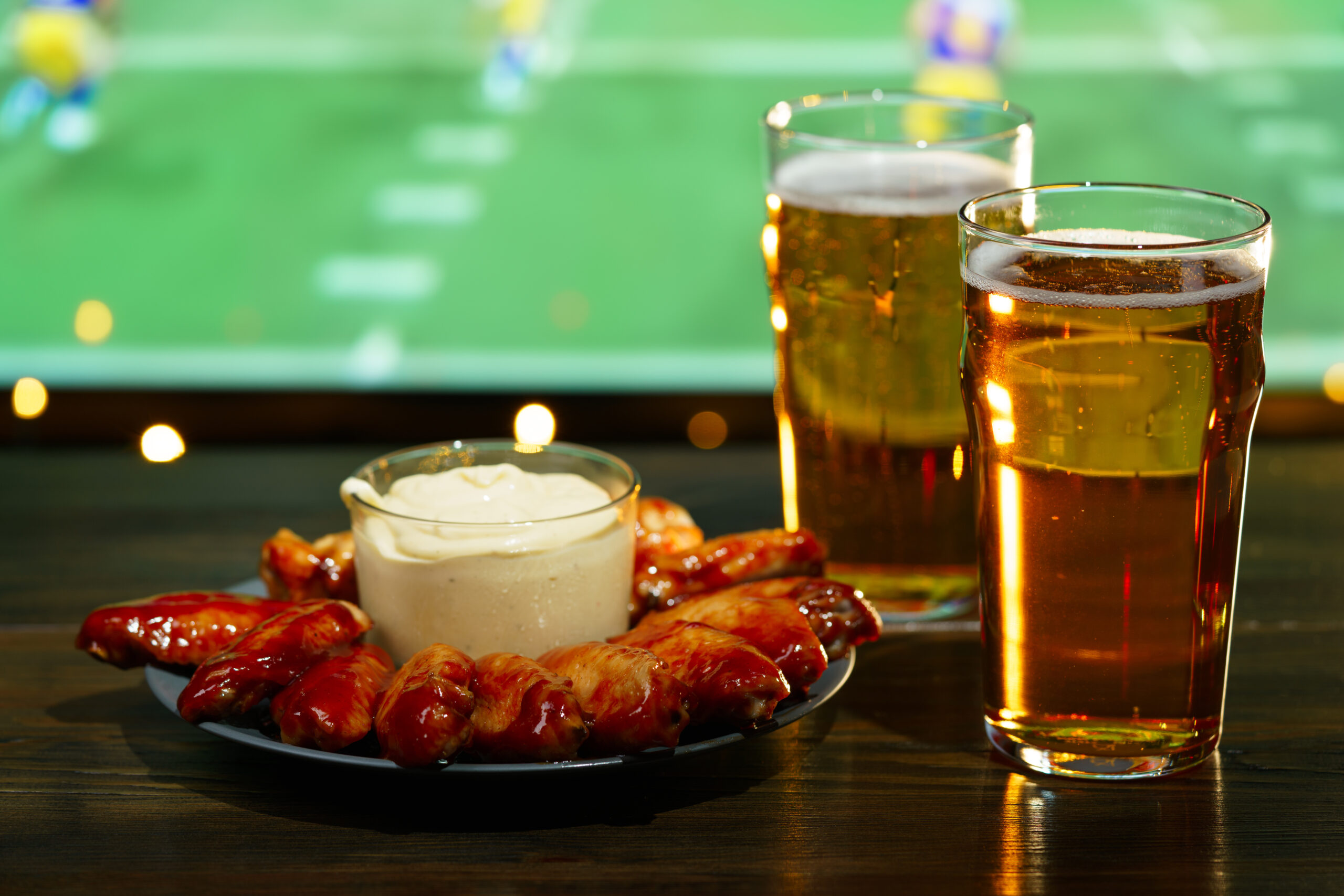 beer and chicken wings in front of a game of football on the TV.