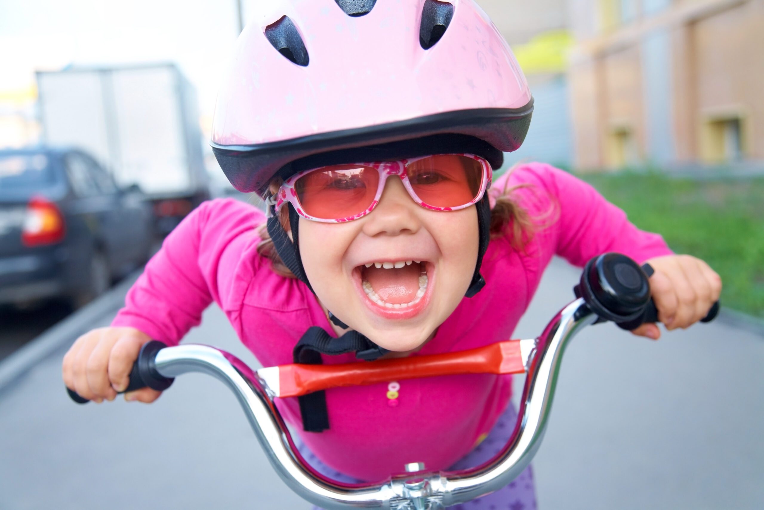 A young bike rider in pink sweater, glasses and helmet laughs at the camera.