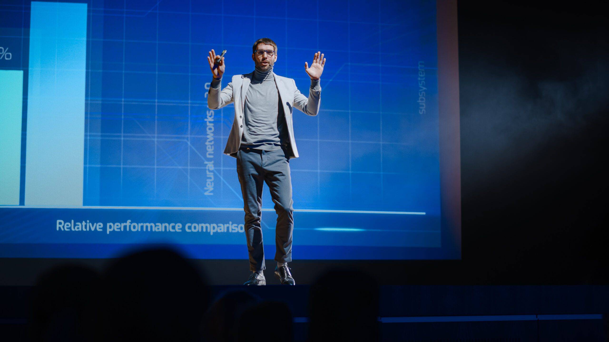 Man stands on a stage with a battery-powered laser pointer in his hand in front of a blue background.